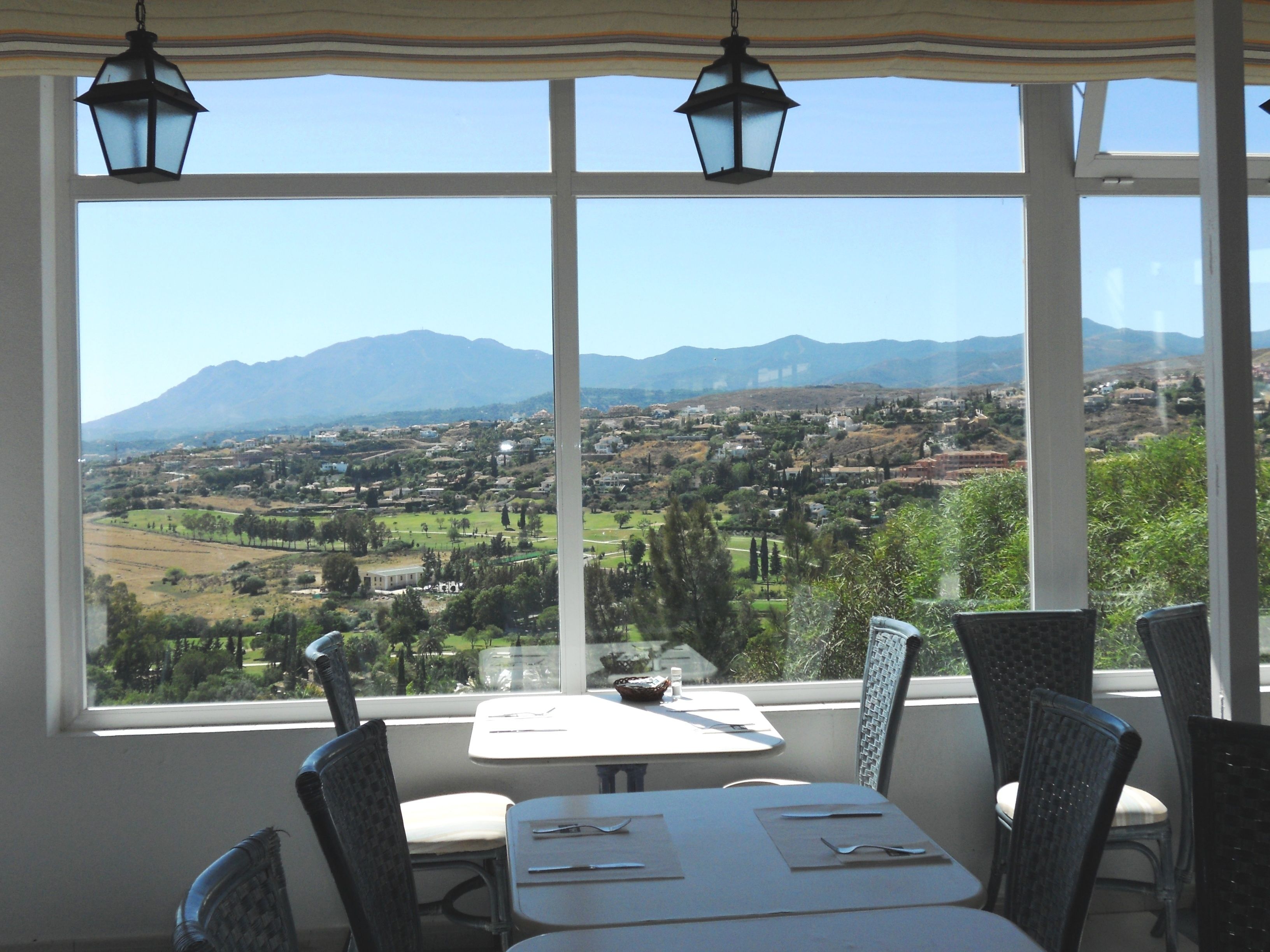 Comedor con mesa y sillas, ventanas amplias con vistas a un pueblo y montañas.