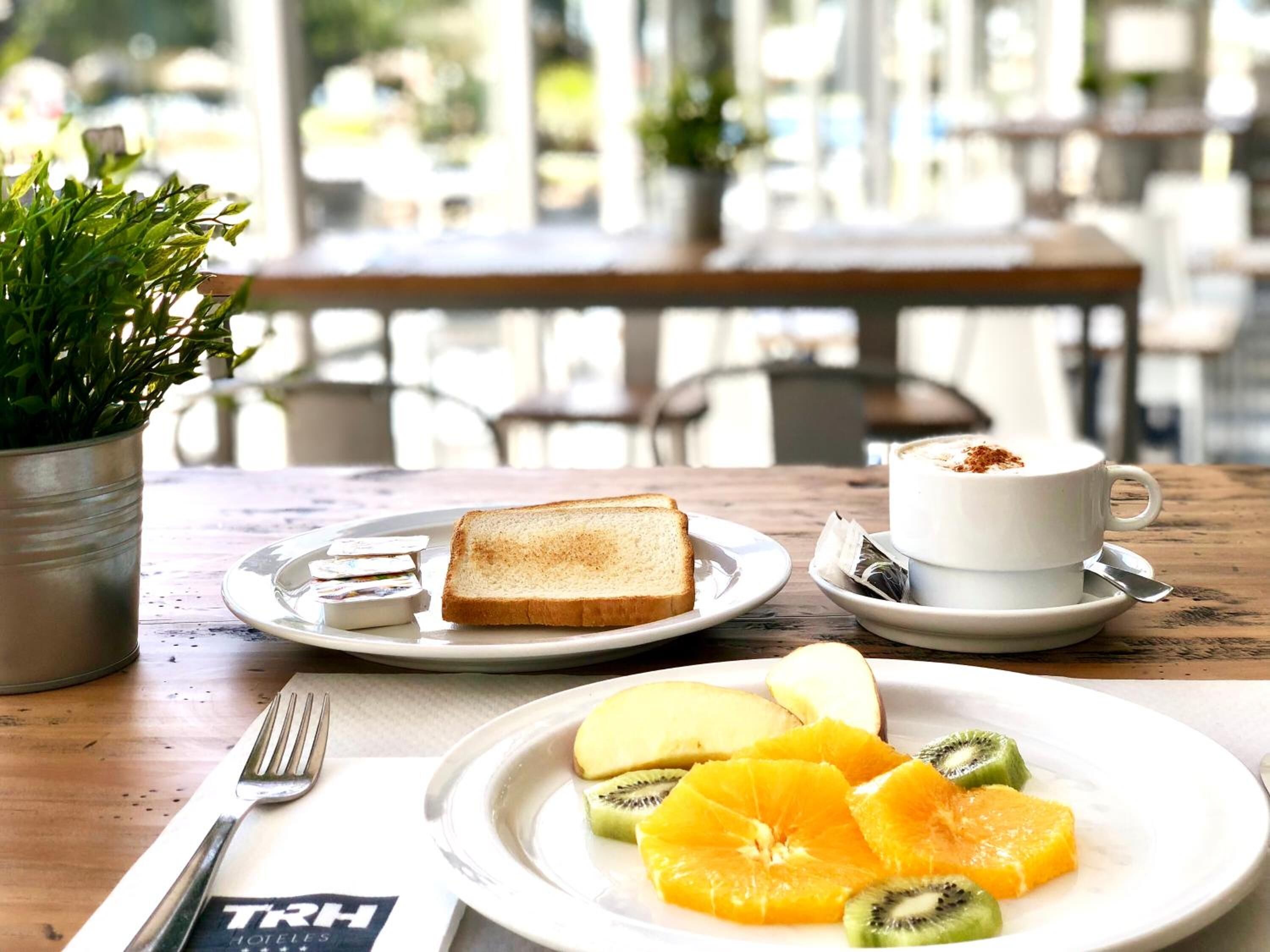 A breakfast setting with a plate of toast, fruit, and a cup of coffee on a wooden table.