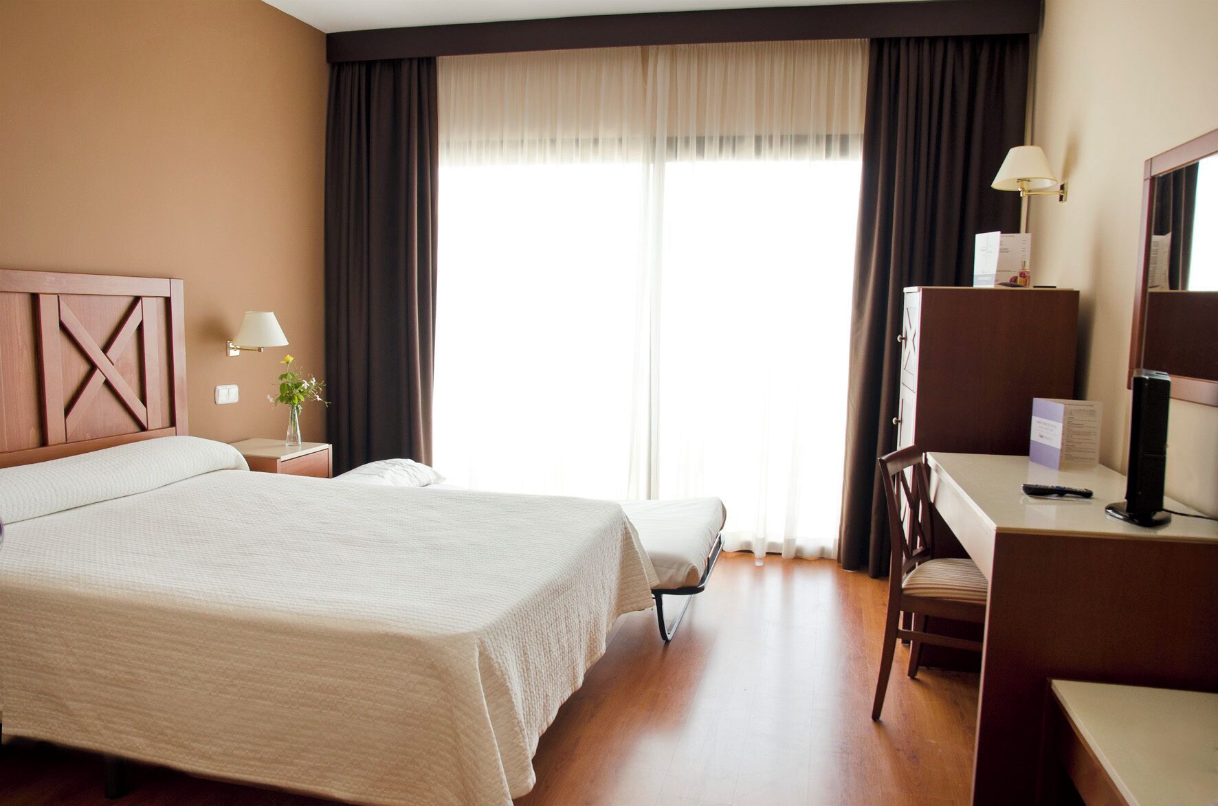 Een hotelkamer met een groot bed, een bureau met stoel, een lamp en een televisie.