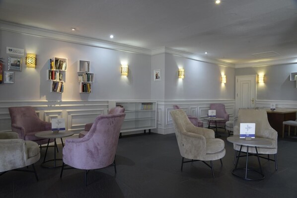A modern lounge area with plush seating, bookshelves, and wall-mounted lighting.