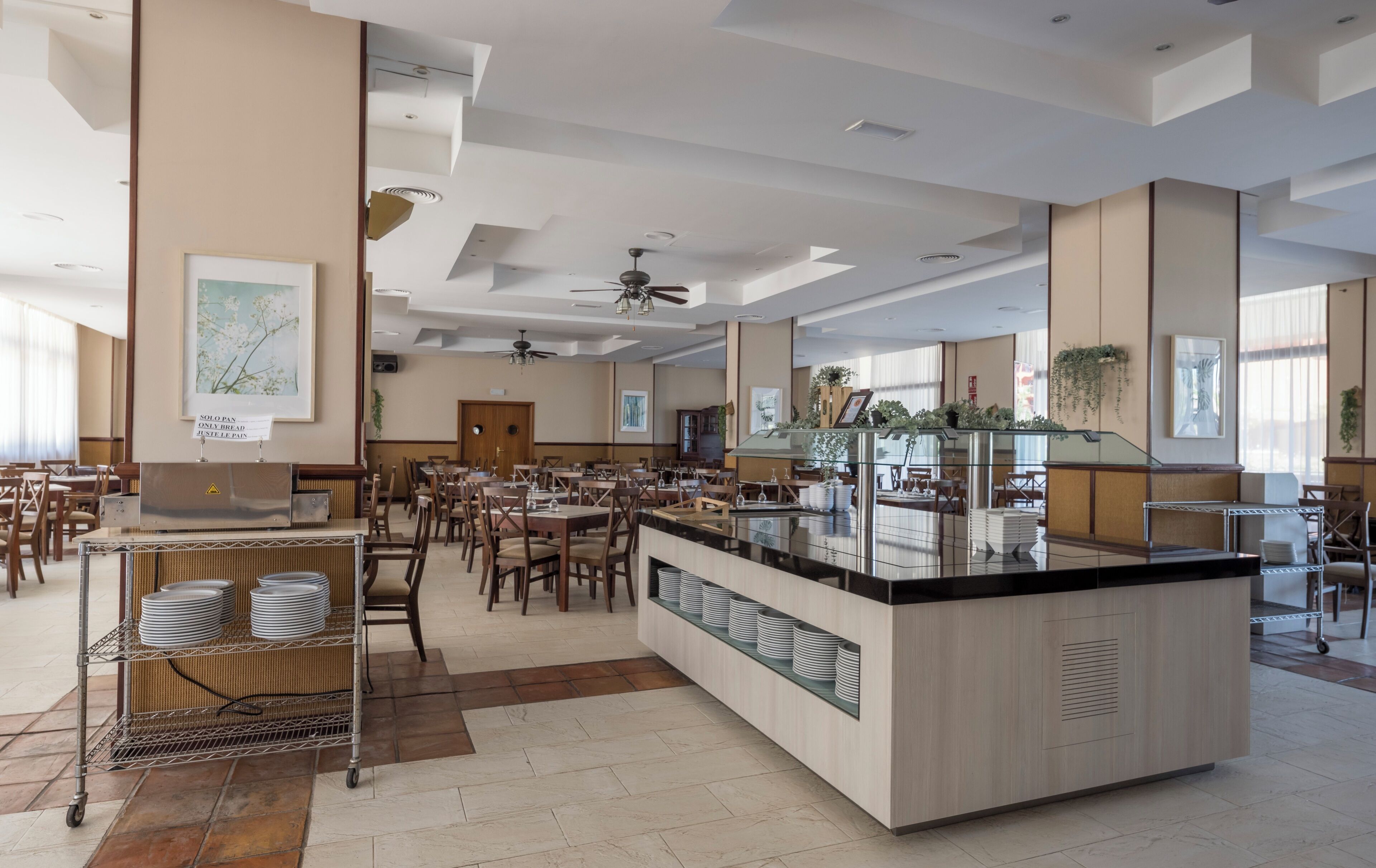 A spacious dining area with multiple tables and chairs, a central counter with a glass display, and ceiling fans.