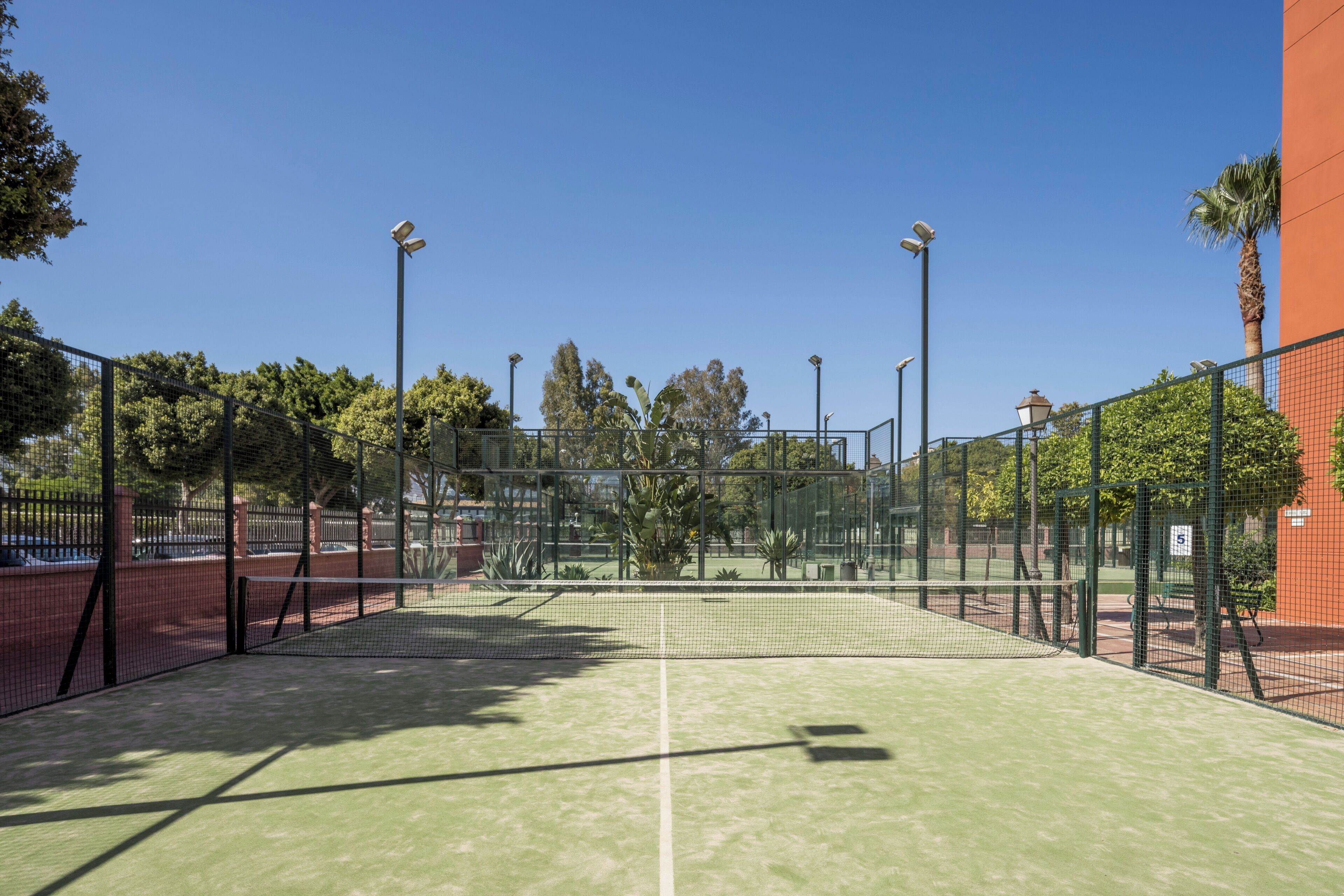 A tennis court with a net, surrounded by a fence, and trees in the background.
