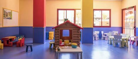 Ein Kinderspielbereich mit einem hölzernen Spielhäuschen, Tischen, Stühlen und bunten Spielsachen.