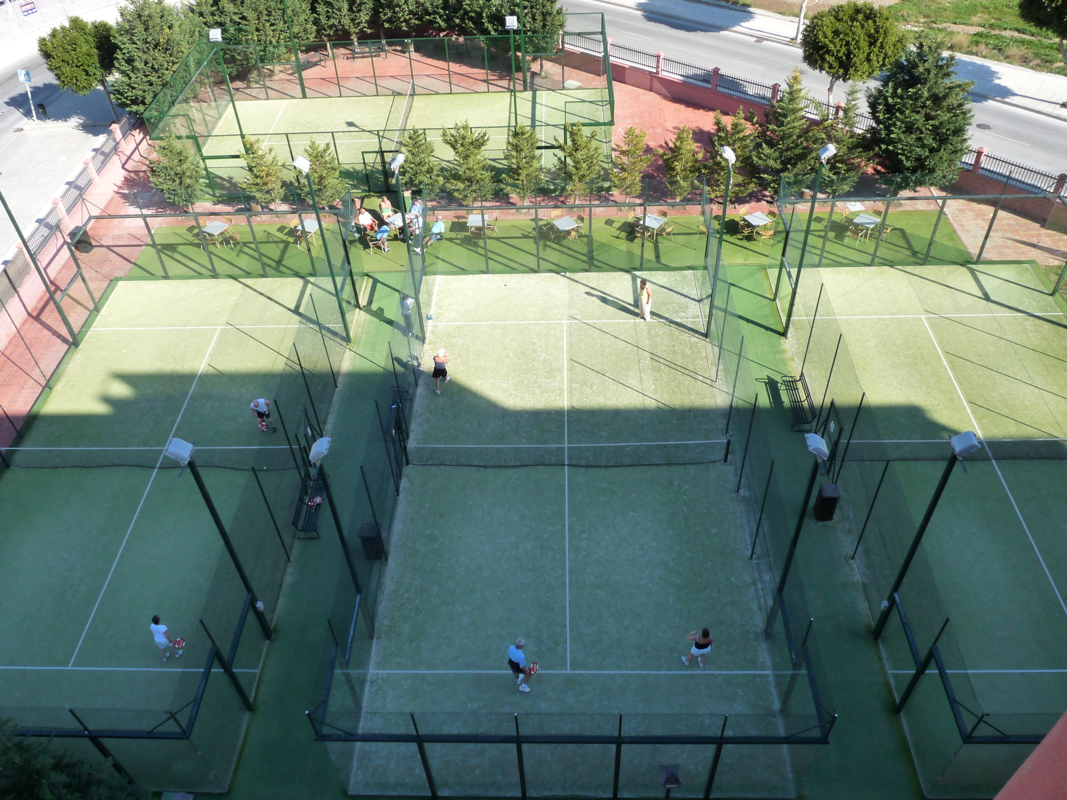 En vy från ovan av ett tennisanläggningsområde med flera banor, sittplatser och träd.