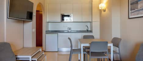 A compact living space with a kitchenette, a flat-screen TV, a dining table with chairs, and a sofa.