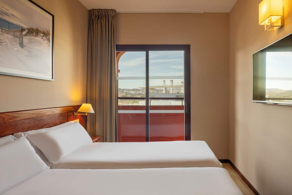 Habitación de hotel con cama, un cuadro en la pared, una ventana con vistas y una lámpara.