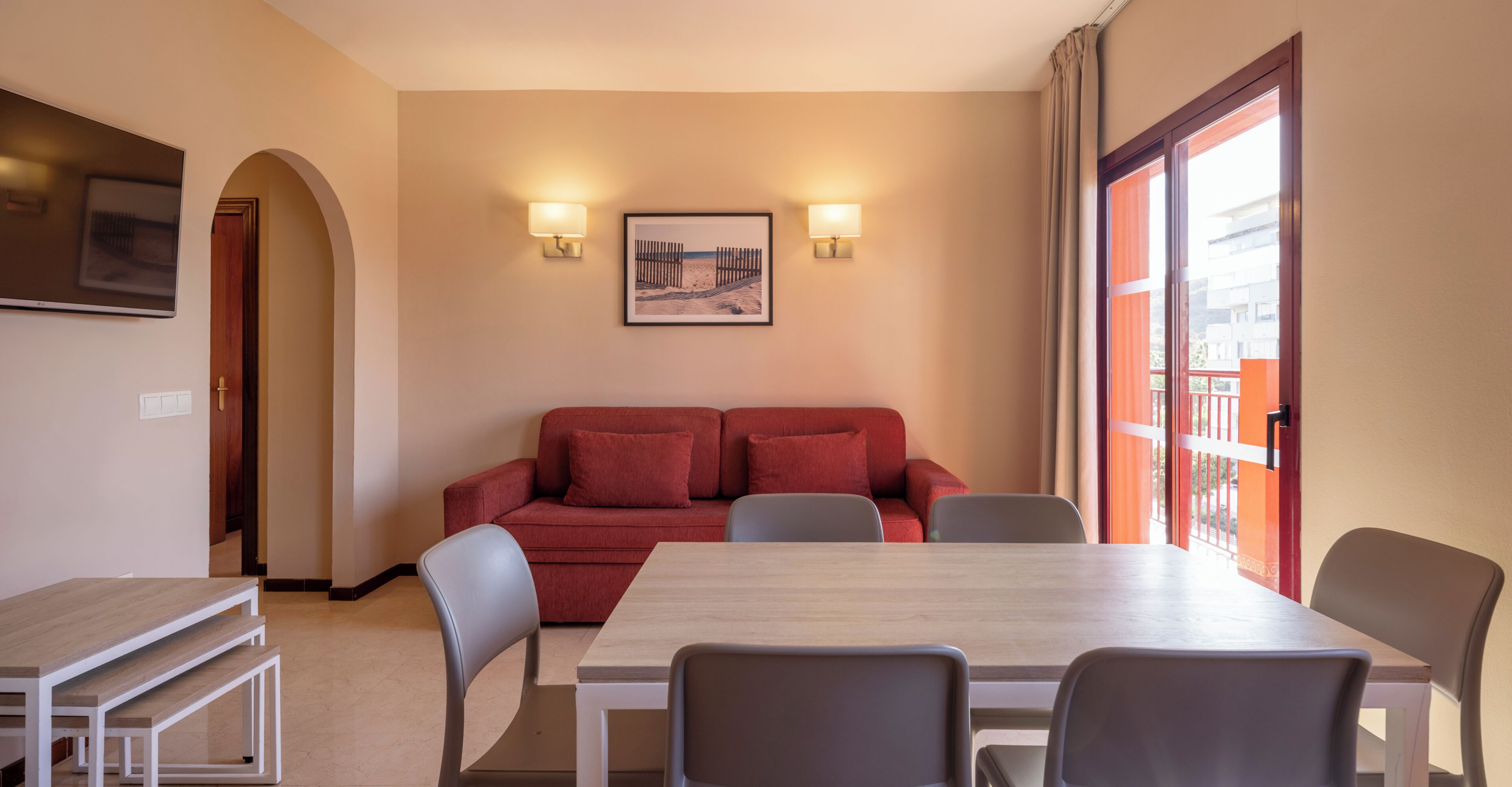 Una habitación con una mesa de comedor, sillas, un sofá rojo y dos lámparas de pared.