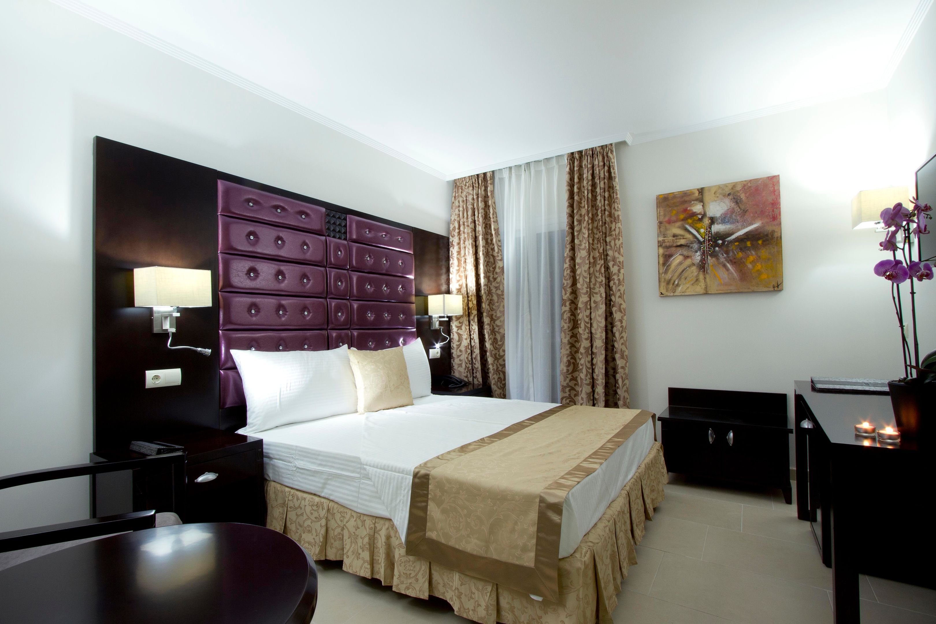 Une chambre d’hôtel avec un grand lit, un bureau, une chaise, une table de chevet et un tableau au mur.