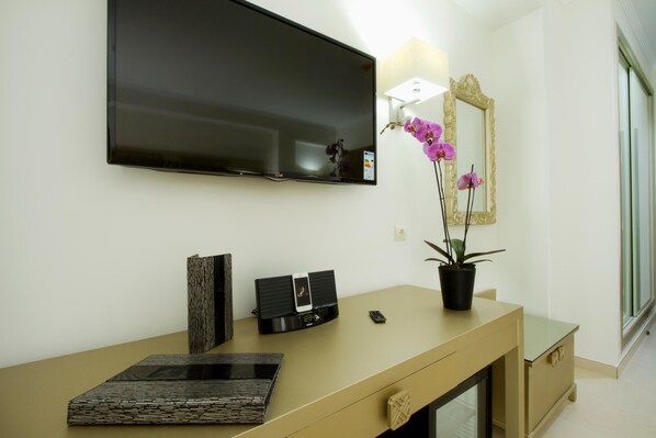 A hotel room with a flat-screen TV mounted on the wall, a bedside table with a lamp, a mirror, and a potted orchid. - Bluesea Alboran (Torremolinos)