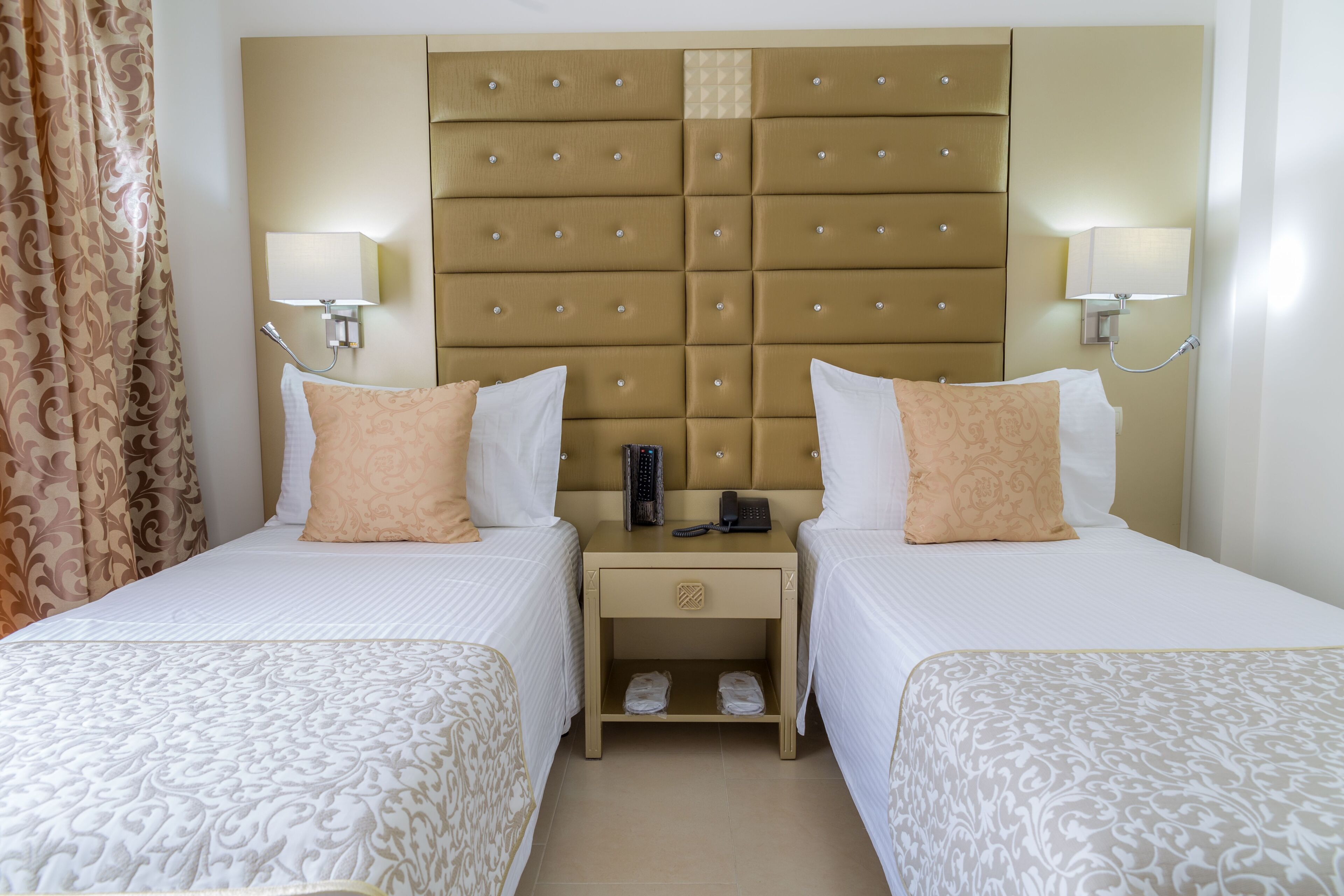A hotel room with two beds, a headboard with a phone and remote, and bedside lamps.