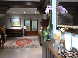 Un vestíbulo amplio con un espejo grande, un banco de madera, un tapete rojo estampado y una figurita decorativa de perro.