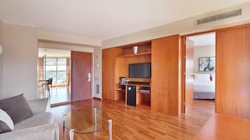 A modern living room with a glass coffee table, a sofa, a flat-screen TV, and a kitchen area with wooden cabinets.