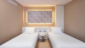 A hotel room with two single beds, a small bedside table, a wall-mounted air vent, and a patterned window.