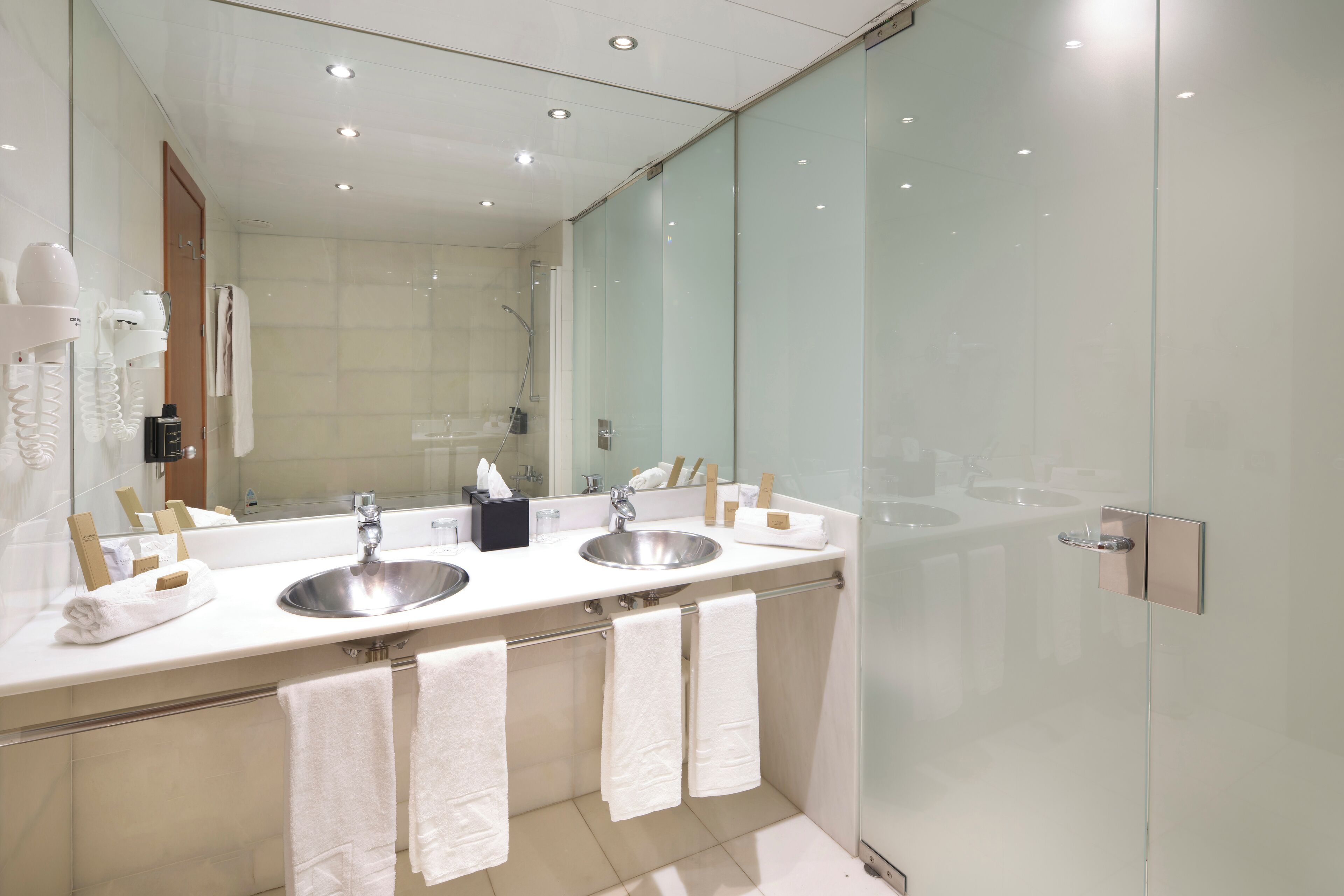 Un baño moderno con dos lavamanos, un espejo grande y cabina de ducha con mampara de vidrio.