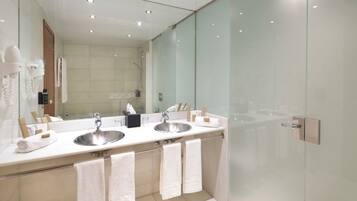 Un baño moderno con dos lavamanos, un espejo grande y cabina de ducha con mampara de vidrio.
