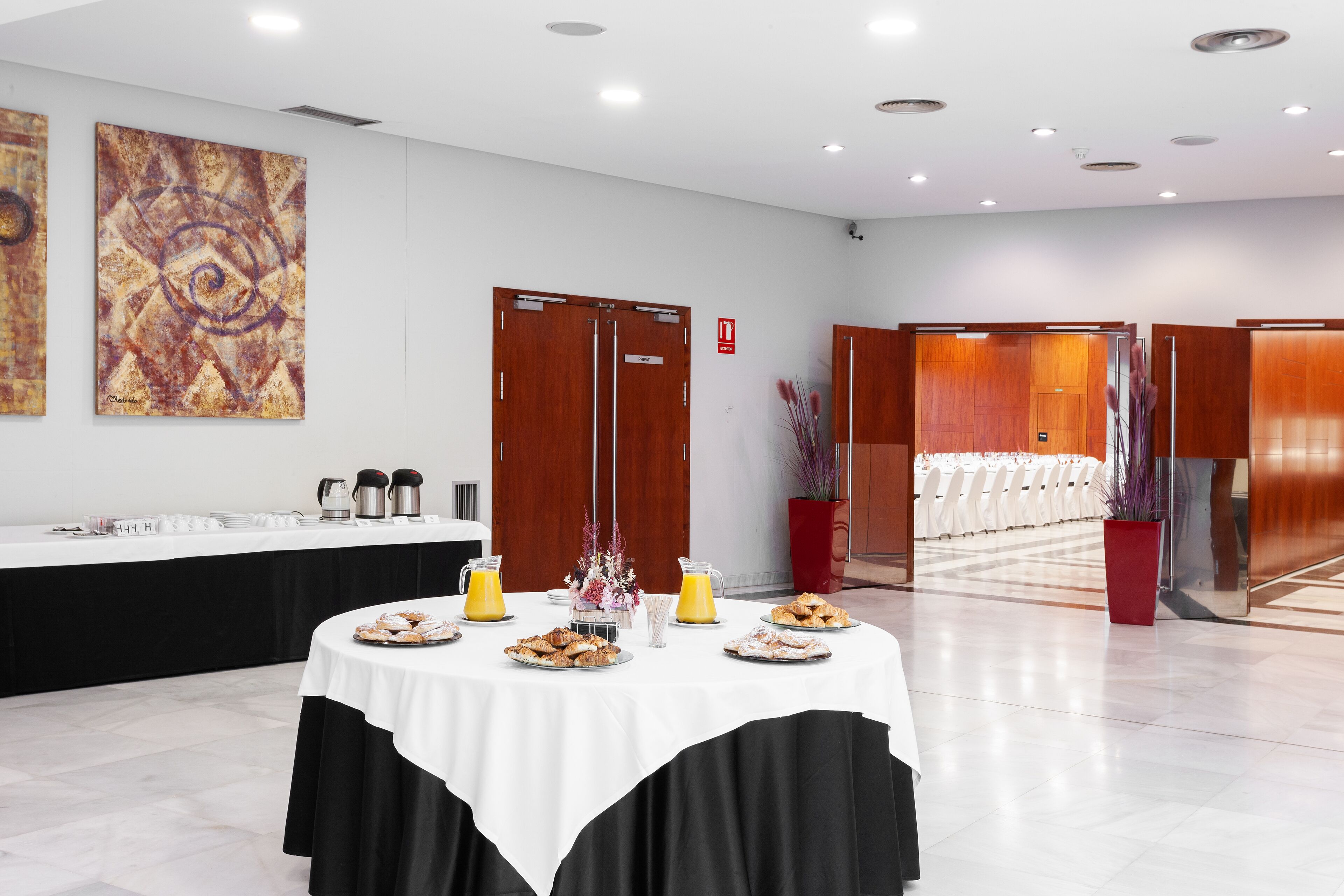 Une salle de conférence avec une table blanche dressée pour le petit-déjeuner, un coin café et un grand tableau abstrait accroché au mur.