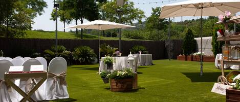 An outdoor wedding setup with white chairs, tables, and string lights.