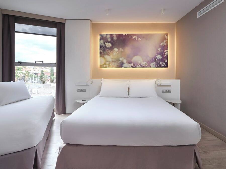 A hotel room with a large bed, two bedside tables, a wall-mounted artwork, and a window with a view.