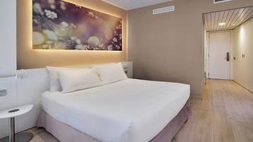 Ein Hotelzimmer mit einem großen Bett, einem Nachttisch, einem Wandbild und einer Tür zu einem anderen Raum.
