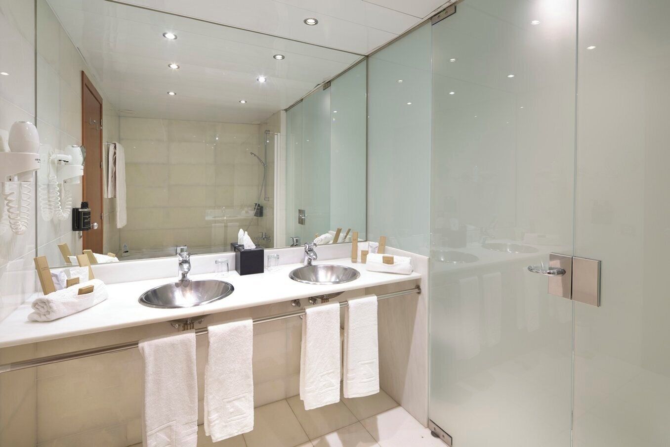A modern bathroom with two sinks, a large mirror, and a glass shower enclosure.
