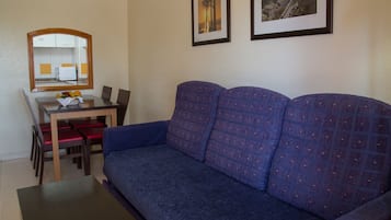 Un salon avec un canapé bleu, une table à manger avec des chaises rouges et un miroir qui reflète la cuisine.