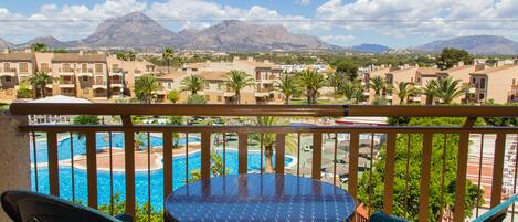 A balcony with a view of a swimming pool, palm trees, and mountains in the background.
