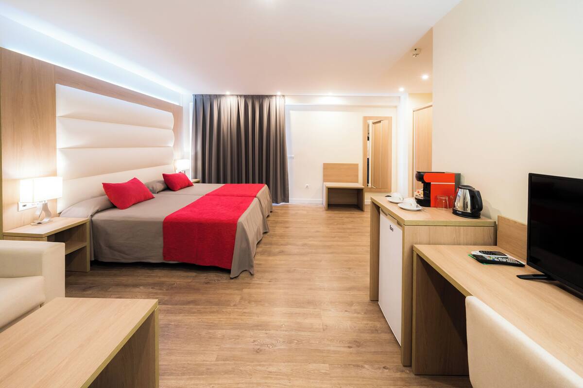 Une chambre d’hôtel moderne équipée d’un lit, de tables de chevet, d’un bureau avec une machine à café, d’une télévision et d’une armoire.