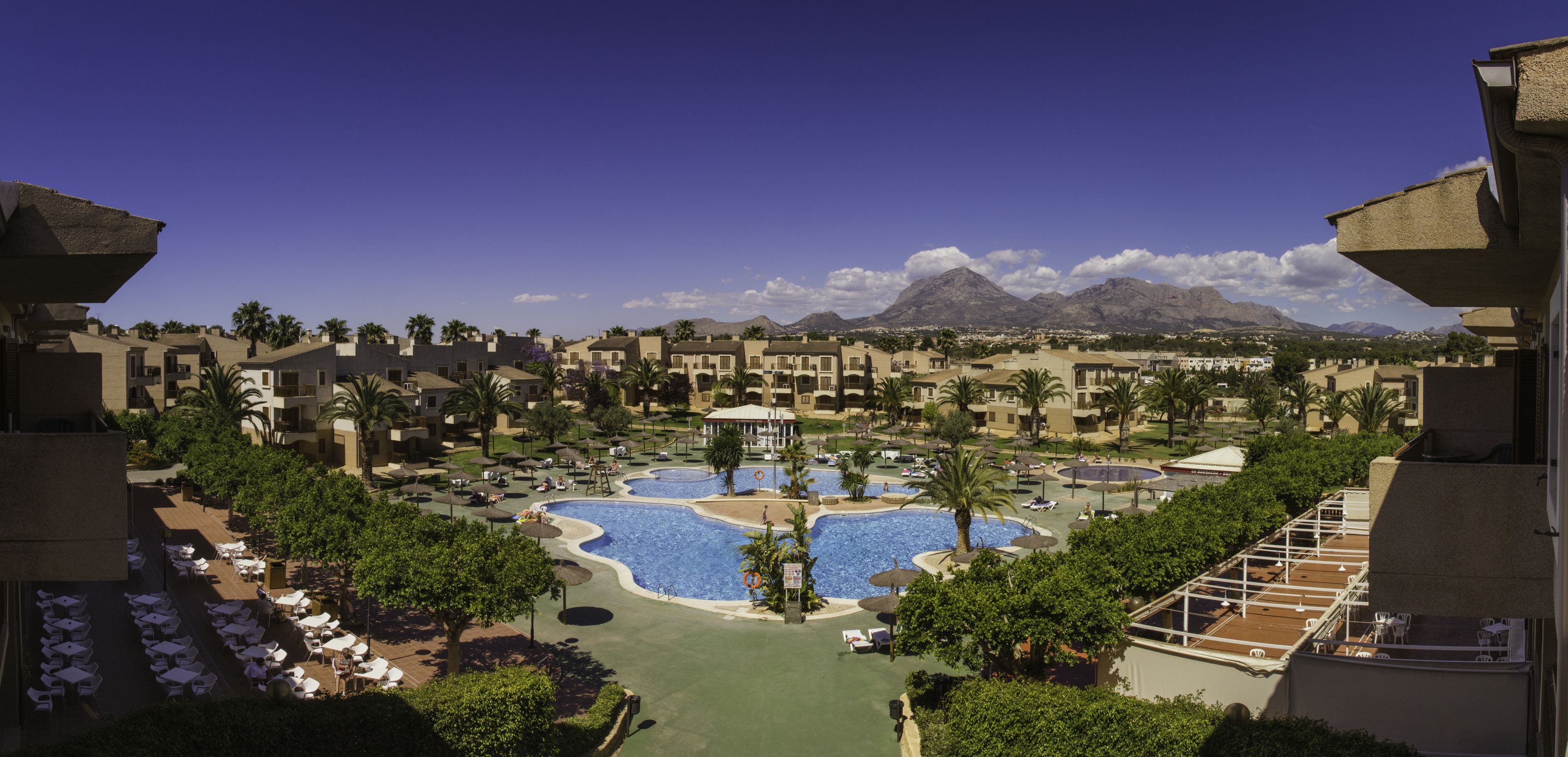 A resort with multiple swimming pools, palm trees, and a mountain backdrop.