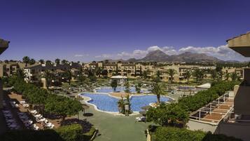A resort with multiple swimming pools, palm trees, and a mountain backdrop.