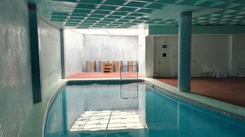 An indoor swimming pool with a tiled floor, a metal ladder, and a white door in the background.