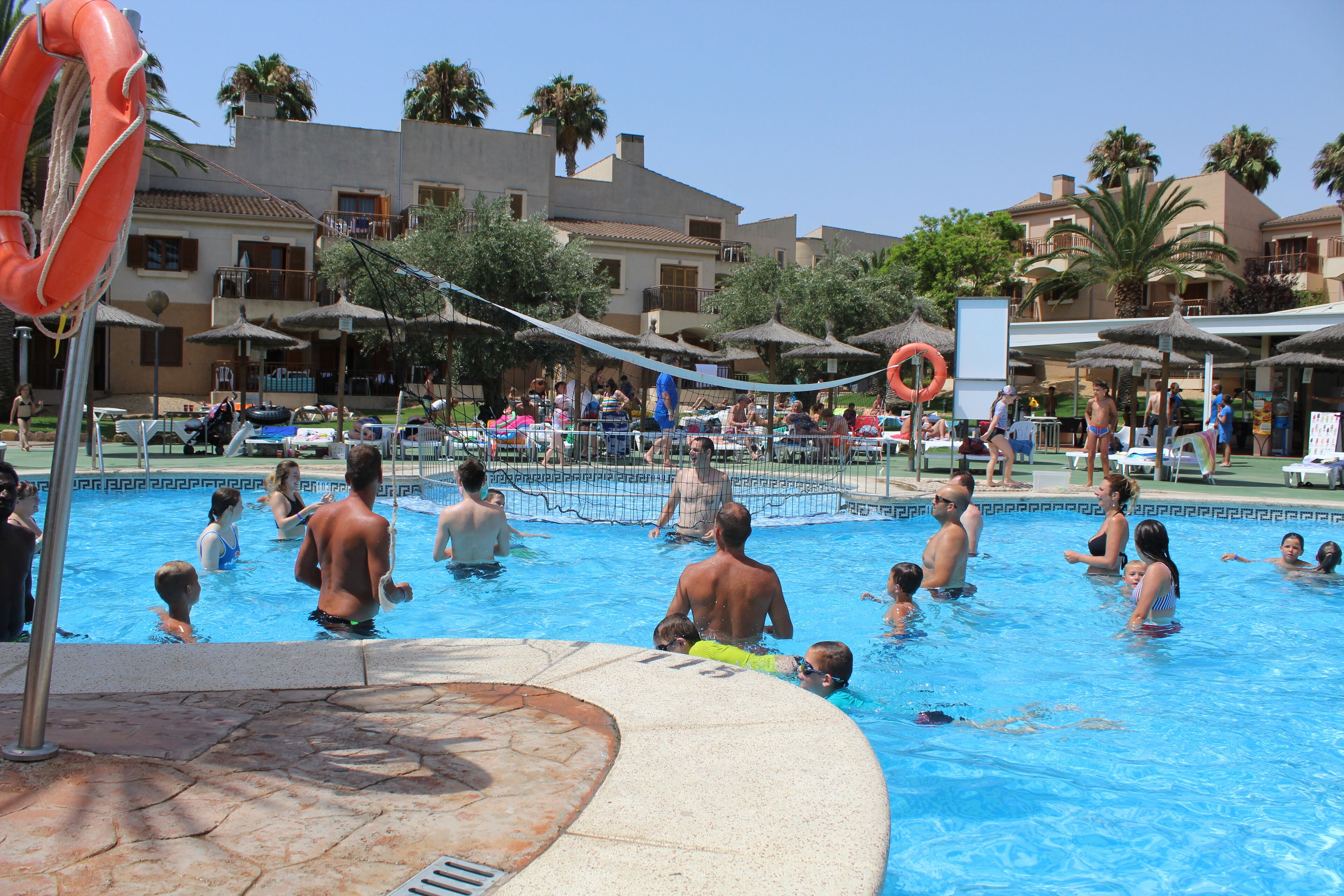 A swimming pool area with multiple people, lounge chairs, umbrellas, and a lifebuoy.