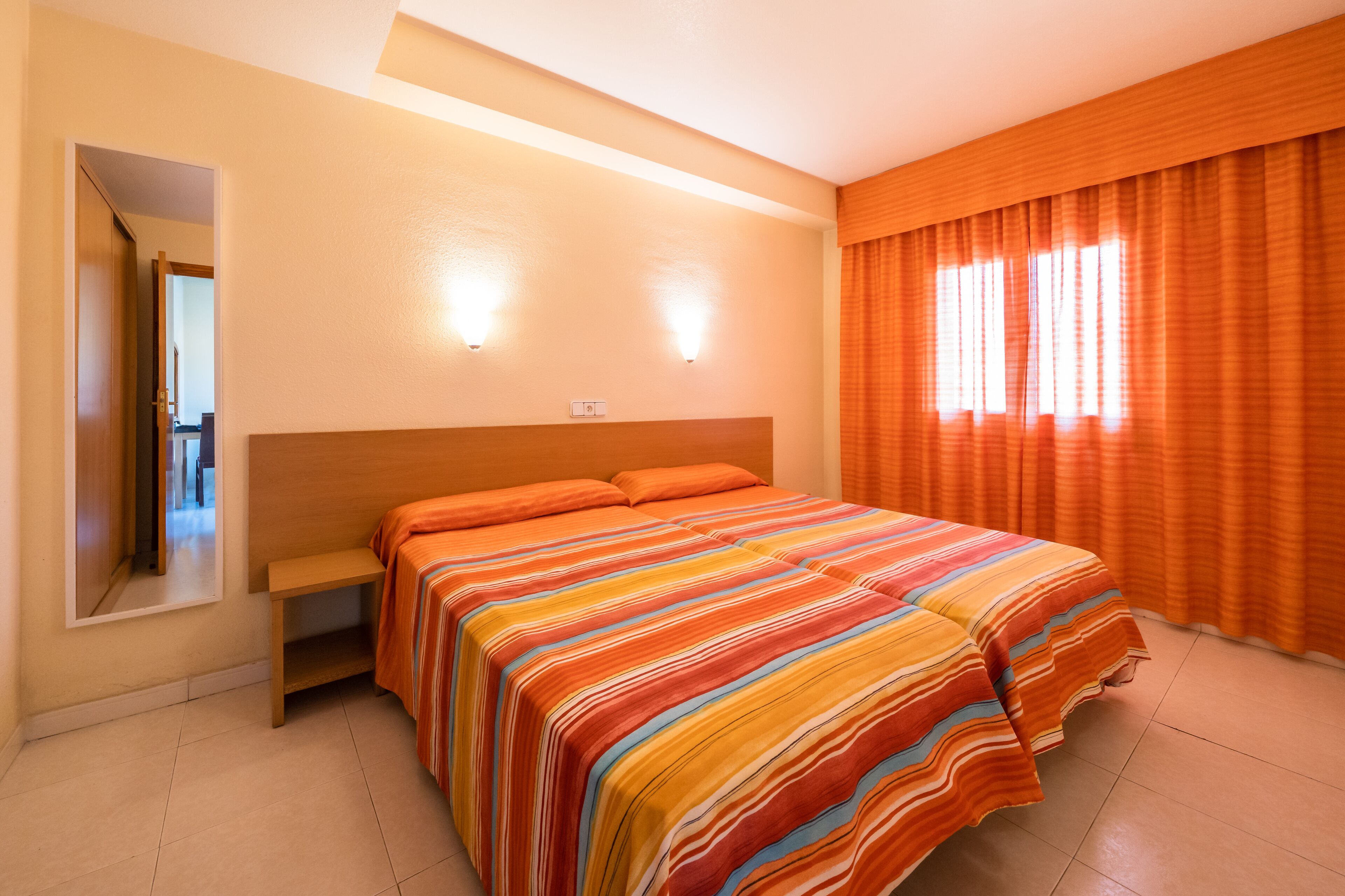 Una habitación de hotel con una cama grande, una mesita de noche, un espejo y una ventana con cortinas.