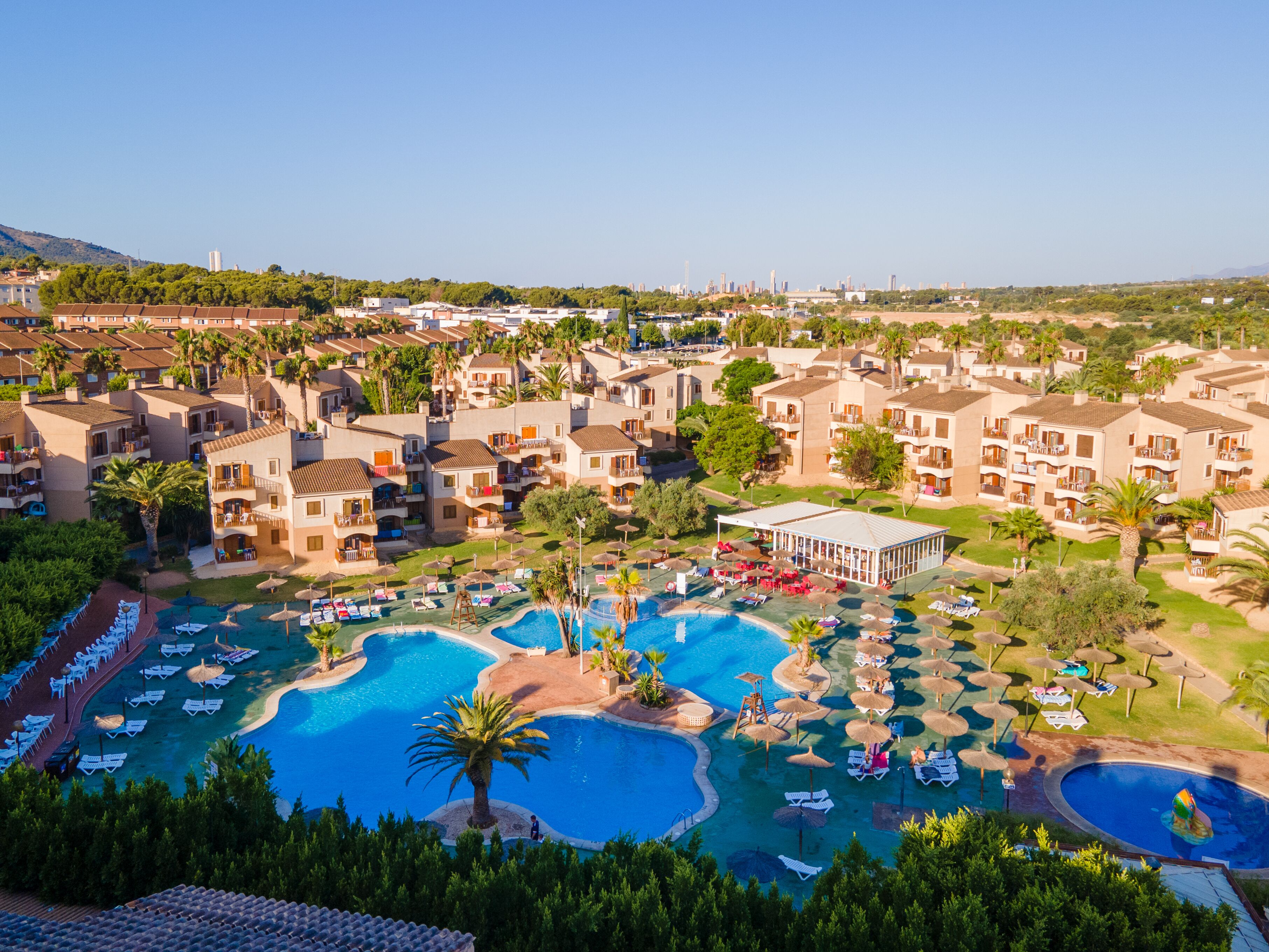 A resort with multiple swimming pools, sun loungers, and a covered area.