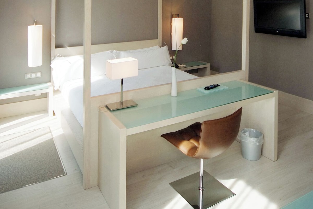 A modern bedroom with a four-poster bed, a glass desk, and a television on the wall.
