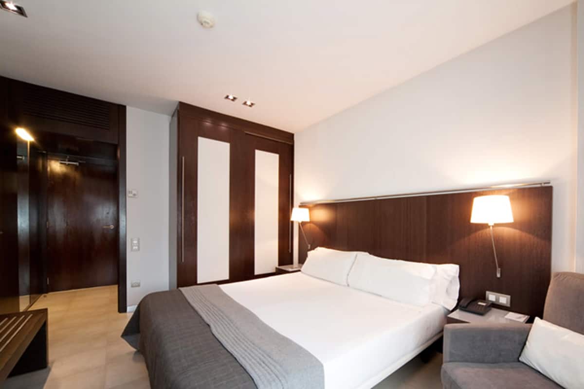A hotel room with a large bed, two bedside tables, a chair, and a wardrobe.