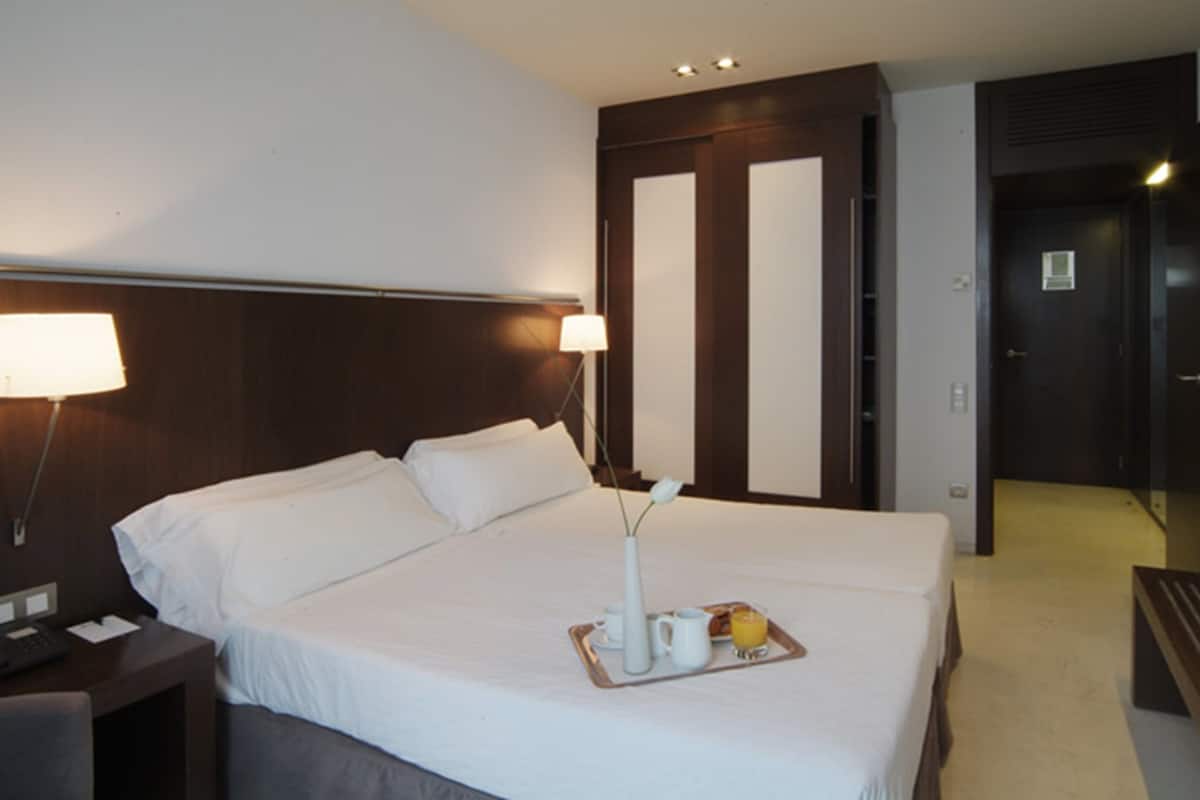A hotel room with a large bed, bedside lamps, a tray with breakfast items, and a door with a mirror.