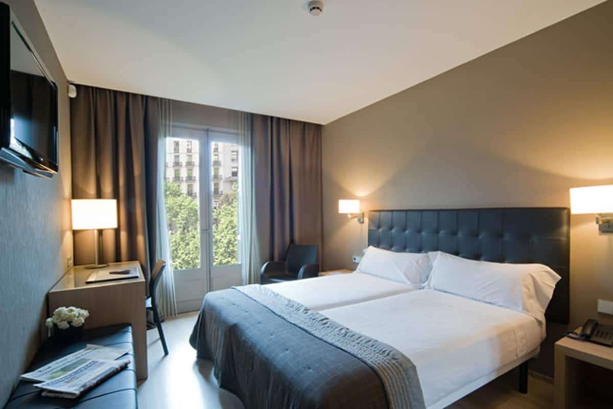 A hotel room with a large bed, a desk with a chair, a TV, and a window with curtains.