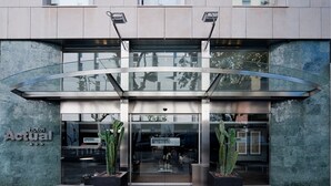 Una entrada de hotel moderna con un toldo de vidrio, grandes cactus en macetas y un cartel que dice 'Actual Hotel'.