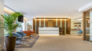 Un espace d’accueil moderne comprenant un comptoir de réception, un coin salon et une grande plante en pot.