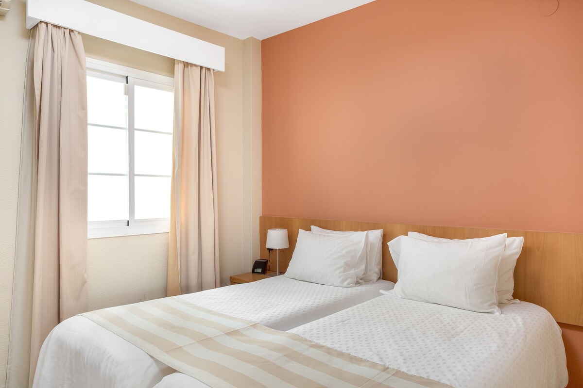 Een hotelkamer met een bed, gordijnen, een nachtkastje en een lamp.