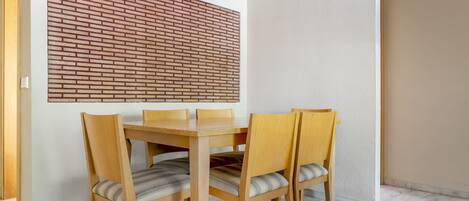 A dining area with a wooden table and chairs, a brick-patterned wall, and a white ceiling light.