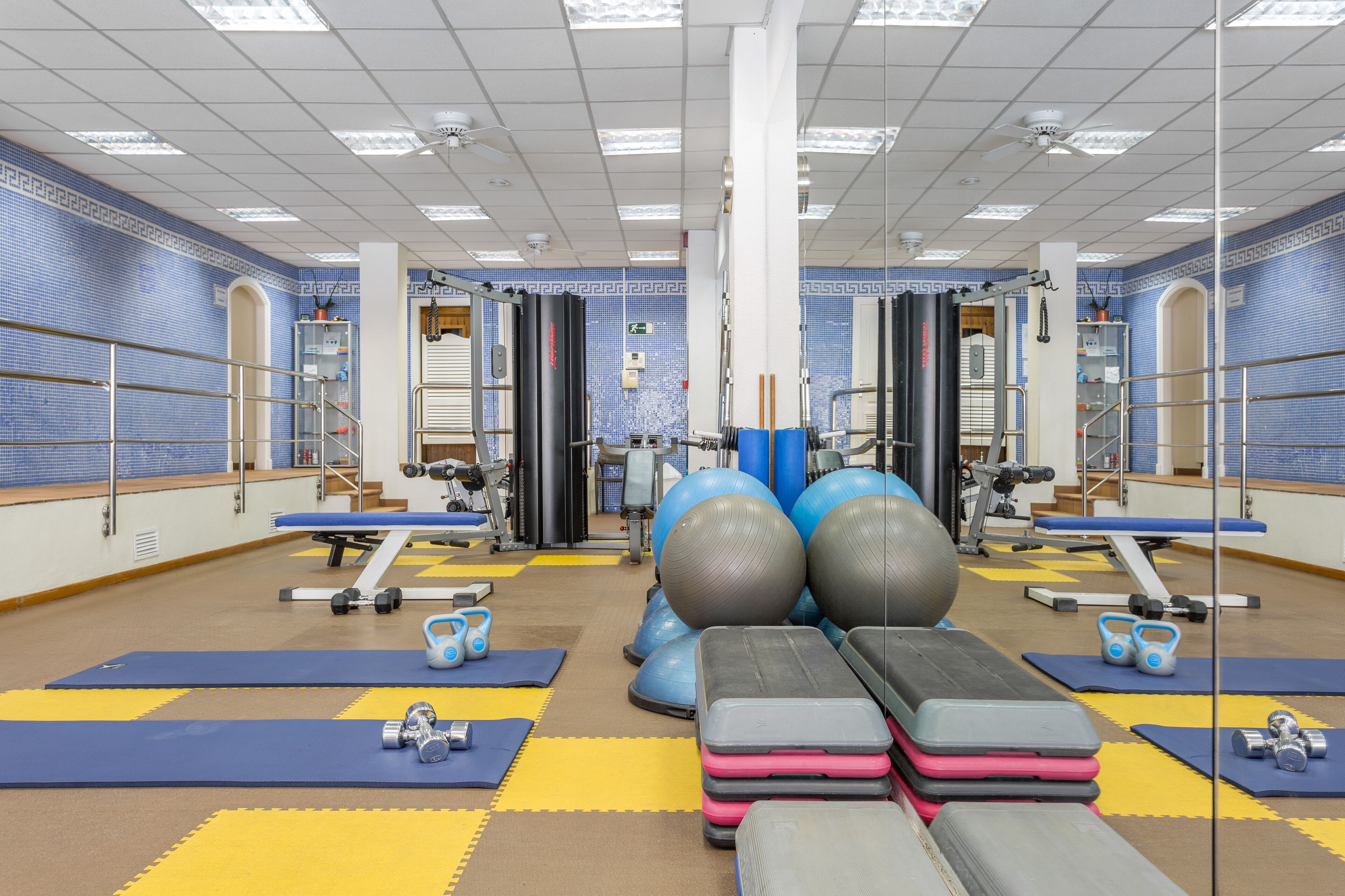 Une salle de sport équipée de matériel d’exercice, de tapis et d’un mur recouvert de miroirs.