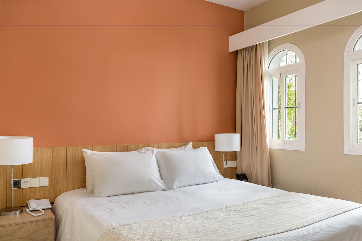 Ein Hotelzimmer mit Bett, Nachttischlampen, Telefon und einem Fenster mit Vorhängen.