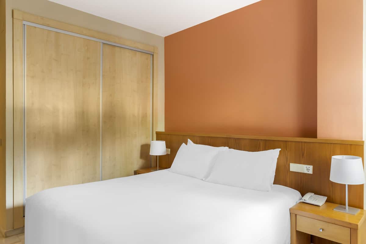 Ein Hotelzimmer mit einem Bett, zwei Nachttischlampen, einem Nachttisch, einem Telefon und einem Holzschrank.