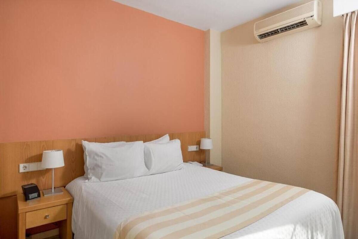 Ein Hotelzimmer mit einem Bett, Nachttischen, Lampen, einer Klimaanlage und einem Vorhang.