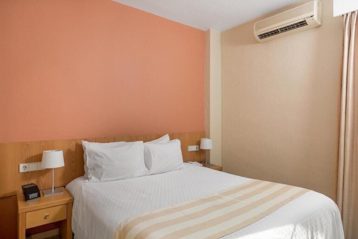 Een hotelkamer met een bed, nachtkastjes, lampen, een airconditioning en een gordijn.