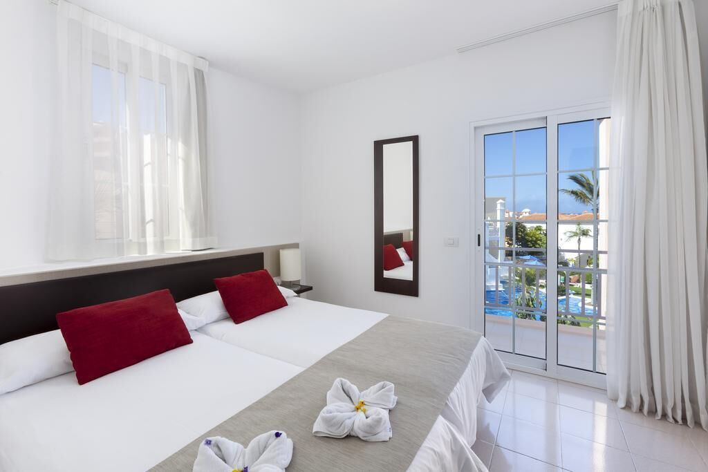 A hotel room with a bed, a large mirror, and a view of a pool through a sliding glass door.
