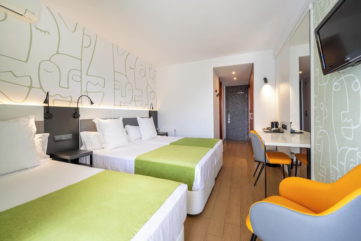 Habitación de hotel con dos camas, un escritorio, una silla y un televisor.