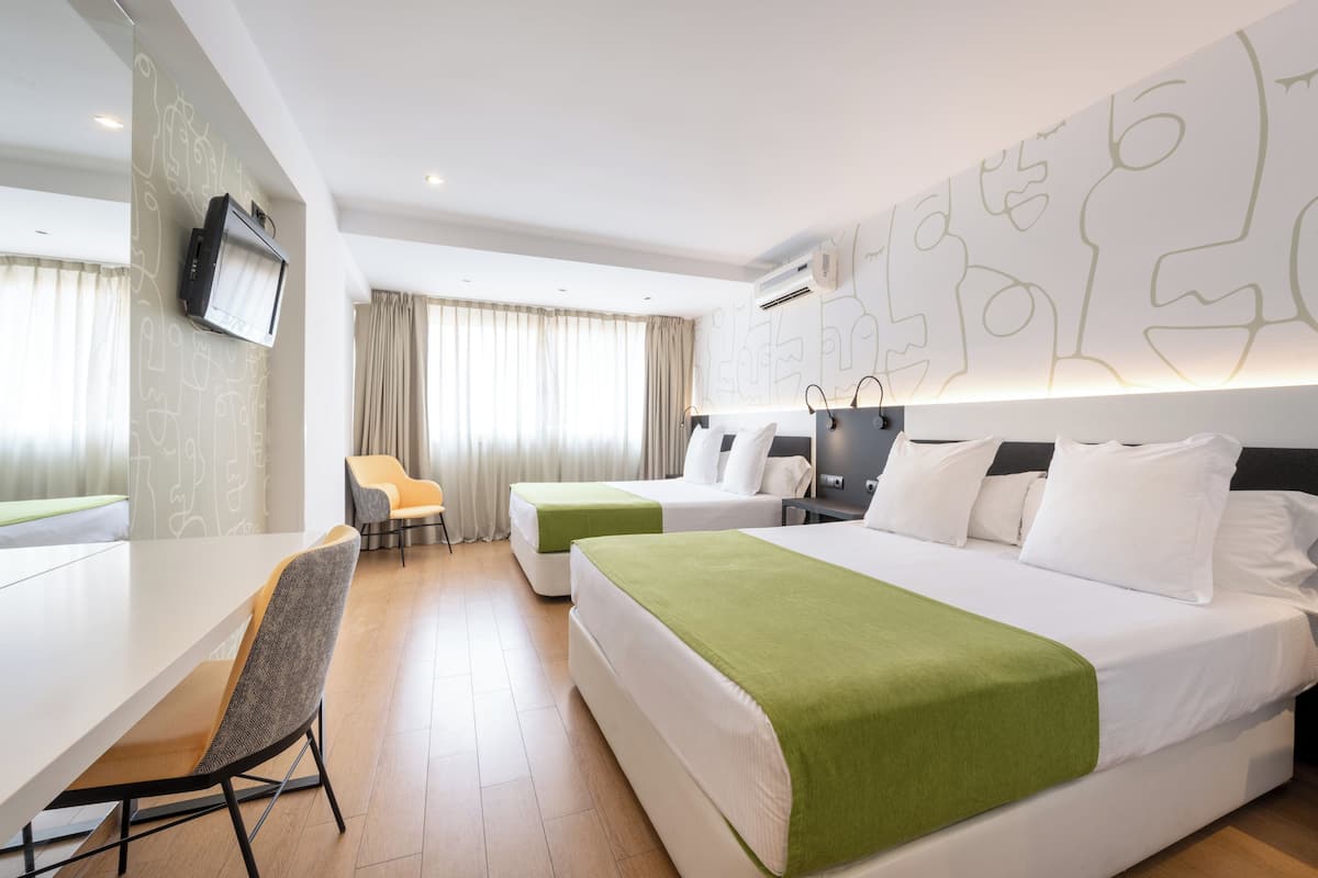 Habitación de hotel con cama, escritorio, silla y televisor montado en la pared.