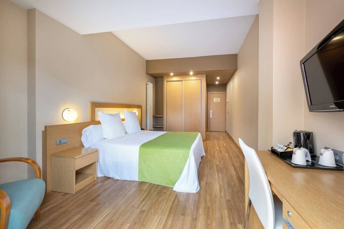 Una habitación de hotel con cama, mesita de noche, silla, escritorio y televisor.